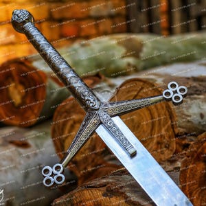 May include: A silver and gold sword with a decorative hilt and a cross guard. The sword is resting on a pile of wooden logs.