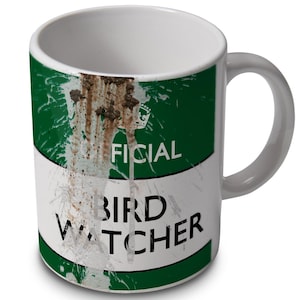 May include: White ceramic mug with a green and white design. The mug has a brown stain on the front and says "Official Bird Watcher" in black text.