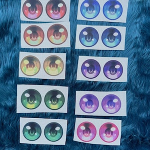 May include: Ten pairs of circular anime-style eye decals arranged in two columns. The pairs feature various gradient colours including red, blue, yellow, green, purple, and pink, each with a white highlight and a dark pupil on a white mesh background.