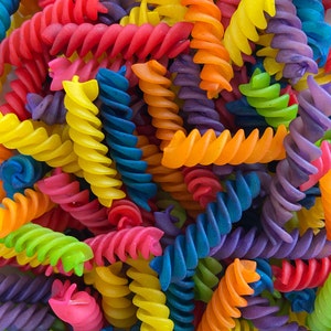 Puede incluir: Primer plano de pasta fusilli cruda multicolor. La pasta en forma de espiral presenta colores vibrantes como rojo, amarillo, azul, verde, naranja y morado. La imagen muestra la pasta en primer plano.