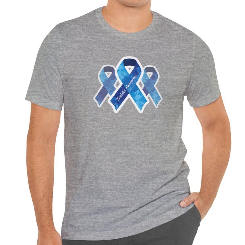 May include: A gray t-shirt featuring three blue ribbons with the words "Diabetes Awareness." The ribbons have a watercolor effect and are outlined in white. The shirt is short-sleeved and has a crew neck.