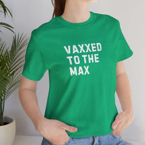 May include: A green t-shirt with the white text "VAXXED TO THE MAX". The shirt has short sleeves and a crew neck. The text is in a bold, distressed font.