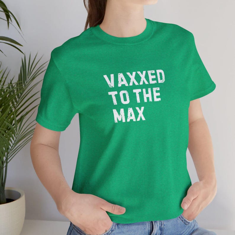 May include: A green t-shirt with the white text "VAXXED TO THE MAX". The shirt has short sleeves and a crew neck. The text is in a bold, distressed font.