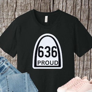 May include: Black t-shirt with a white graphic of a highway sign with the number 636 and the word "PROUD" underneath.