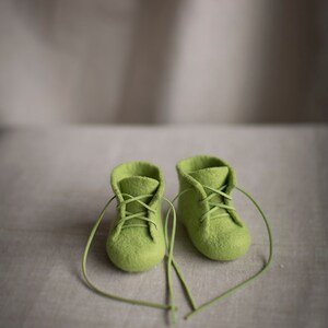 May include: A pair of green felt baby booties with laces tied in a heart shape.