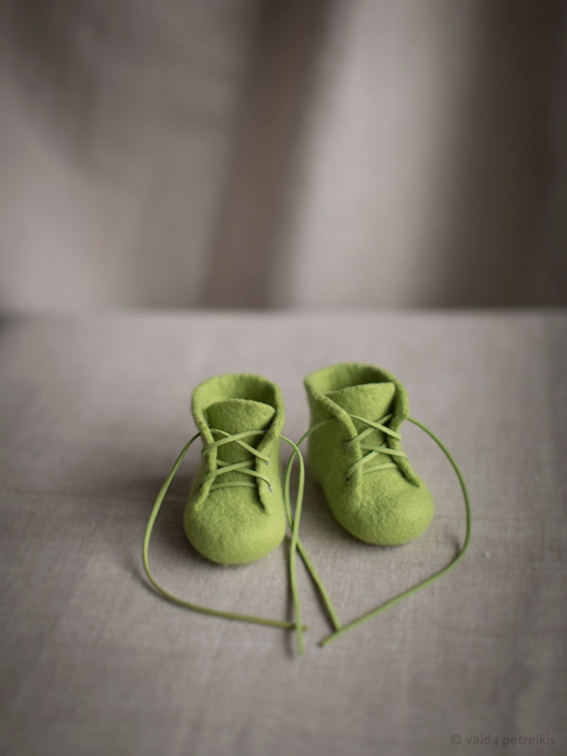 May include: A pair of green felt baby booties with laces tied in a heart shape.