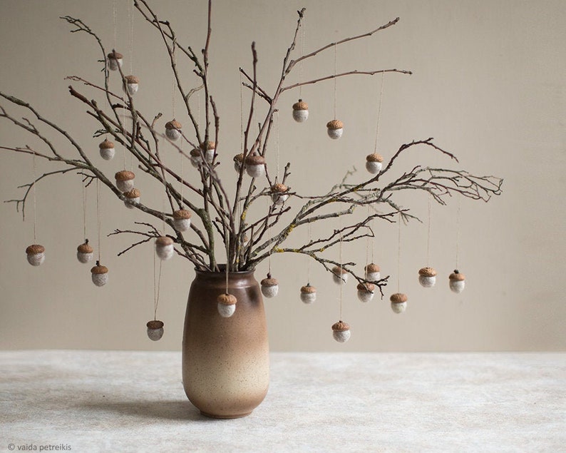 May include: A vase filled with bare branches with small, brown and white acorn ornaments hanging from the branches.