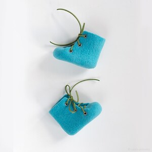 Puede incluir: Dos pares de botines de beb&eacute; de fieltro azul con cordones verdes. Los botines est&aacute;n atados con un lazo.