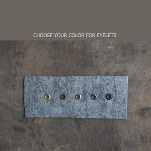 May include: A close-up of five metal eyelets in different colors on a gray felt swatch. The colors are gold, silver, nickel, black, and antique brass.  Choose your color for eyelets.