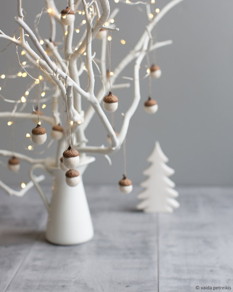 Pu&ograve; includere: Un albero di rami bianchi dipinto con un vaso a forma di brocca bianco e ornamenti di ghianda marroni appesi ai rami. L'albero &egrave; decorato con luci fatate bianche. Un albero di legno bianco ritagliato &egrave; in primo piano.