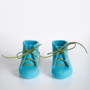 Puede incluir: Un par de zapatos de beb&eacute; de fieltro azul con cordones verdes atados en un lazo.