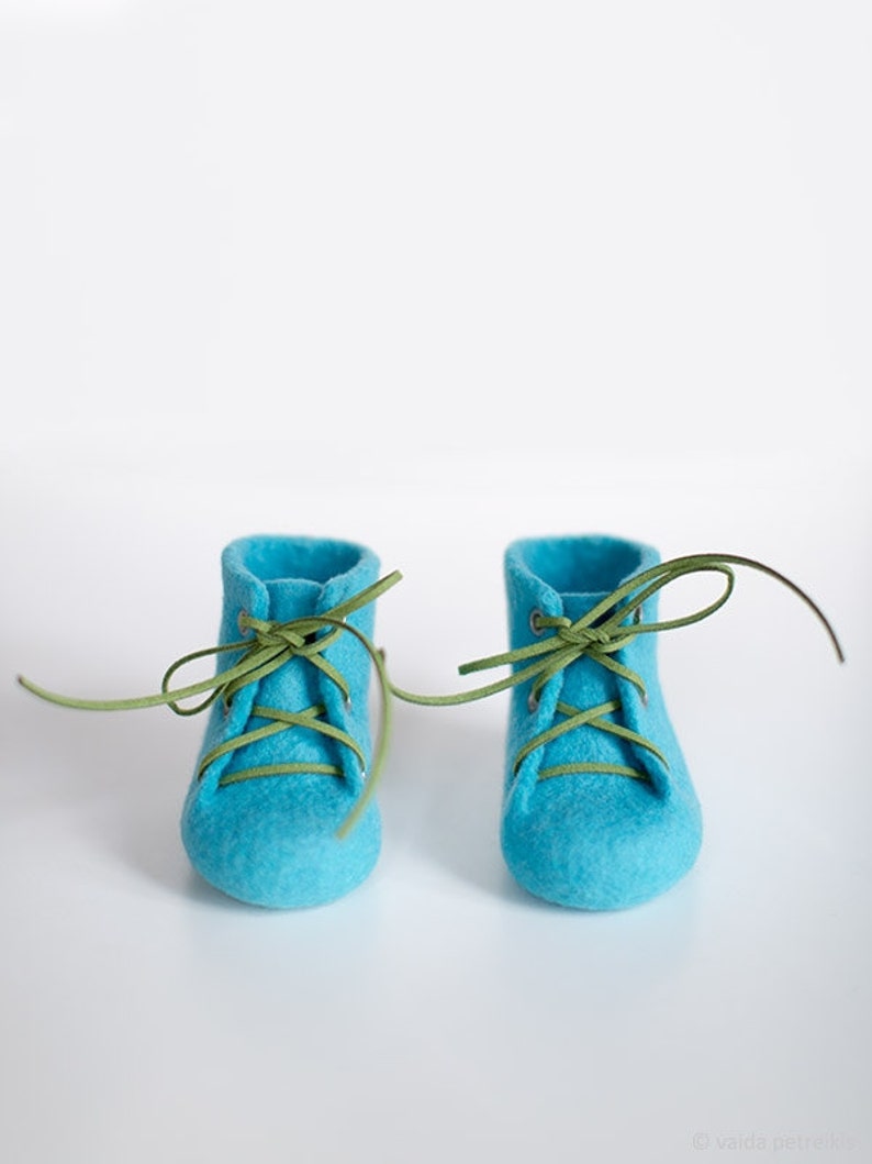 Puede incluir: Un par de zapatos de beb&eacute; de fieltro azul con cordones verdes atados en un lazo.