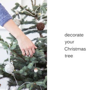 May include: A hand decorates a Christmas tree with white and brown ornaments. The text "decorate your Christmas tree" is on the right side of the image.