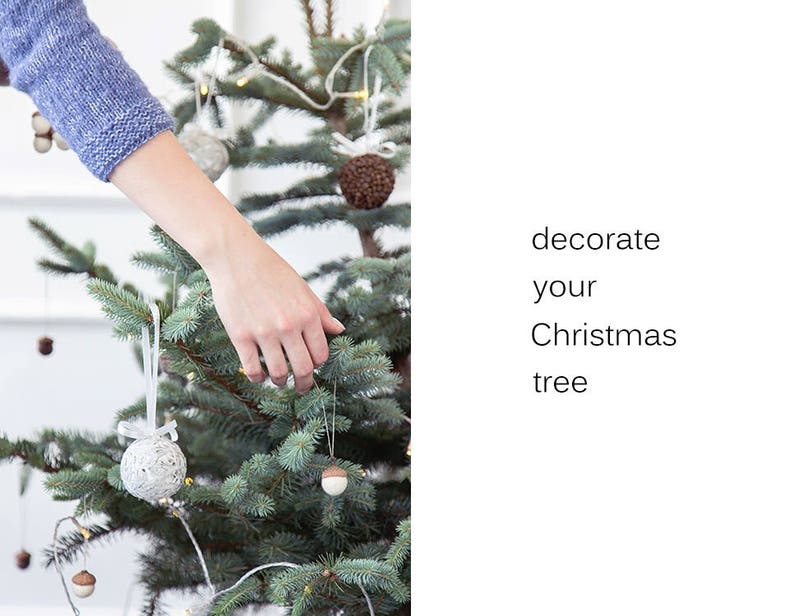 May include: A hand decorates a Christmas tree with white and brown ornaments. The text "decorate your Christmas tree" is on the right side of the image.