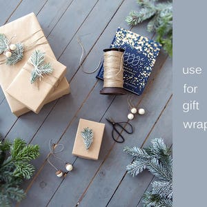 May include: Two brown gift boxes wrapped with twine and decorated with sprigs of greenery and white beads. A third box is partially visible in the background. A spool of twine and a pair of scissors are also visible. The text "use for gift wrapping" is visible in the background.