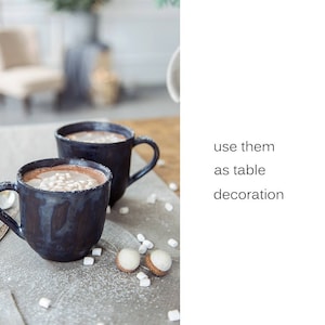 May include: Two mugs of hot chocolate with marshmallows on a table with white decorative balls.  Use them as table decoration.