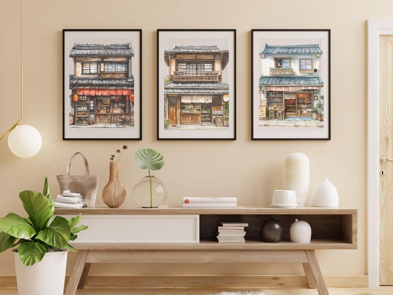 Puede incluir: Tres acuarelas enmarcadas de fachadas de tiendas japonesas con marcos negros. Las pinturas est&aacute;n colgadas en una pared beige sobre un estante de madera con art&iacute;culos decorativos.
