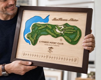 May include: A framed 3D wooden map of the Cypress Point Club golf course in Pebble Beach, California. The map features a light wood background, a blue water element, green fairways, and a scorecard with yardage and par details.