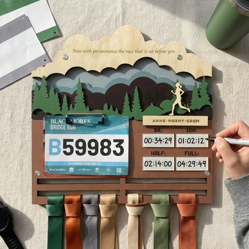 May include: A wooden race medal and bib display rack featuring a layered mountain and forest landscape, a runner silhouette, and the text "Run with perseverance the race that is set before you." Includes a bib clip and slots for race times.