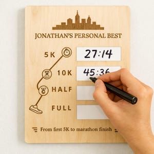 May include: Wooden plaque with the text "JONATHAN'S PERSONAL BEST" and a city skyline silhouette. It features spaces to record running times for 5K, 10K, Half, and Full marathons. The 5K time is 27:14 and the 10K time is 45:36.
