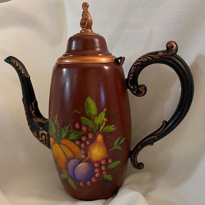 May include: A decorative brown teapot with a copper-coloured lid and accents. The teapot features a painted design of fruits, including a pumpkin, grapes, and plums. The handle and spout are black with copper-coloured detailing.