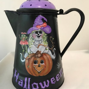 May include: Black metal Halloween-themed coffee pot with a purple lid and handle. The pot is decorated with a smiling ghost holding a pumpkin, a frog, and the word "Halloween" in purple.