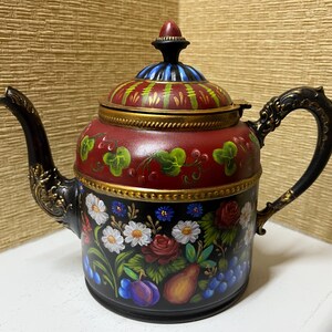 May include: A decorative teapot with a black base and handle, featuring a red body adorned with painted flowers, fruits, and green leaves. The lid is red with green and yellow stripes, and a black finial. The teapot has a gold trim.