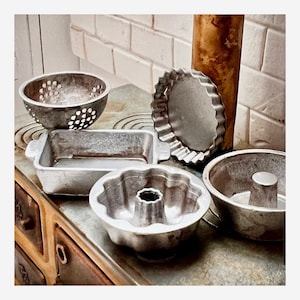 Peut inclure: Un assortiment de moules à pâtisserie en métal vintage, comprenant une passoire ronde, un moule à cake rectangulaire, un moule à tarte cannelé, un moule à bundt et un moule à gâteau rond. Les moules sont de tailles et de formes variées.