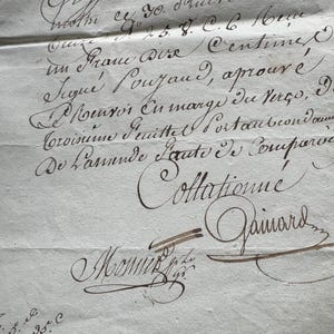 May include: A close-up of a vintage document with elegant cursive handwriting in brown ink. The paper is aged and textured, with visible folds and imperfections. The document features signatures and the word "Collationné".