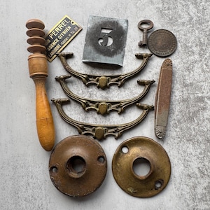 May include: An assortment of vintage hardware and decorative items. Includes brass drawer pulls, a wooden handle, a metal number 5 stencil, a key, a coin, and a metal plate with text.