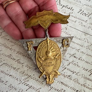 May include: A gold and silver-toned Knights of Pythias badge featuring a triangular frame with the letters F and C, a central oval medallion with a helmet and shield, the text Knights of Pythias and Esto Perpetua, and a top banner bar.