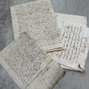 May include: Three pieces of aged, off-white parchment paper featuring dense, handwritten cursive script in dark ink. The papers have uneven, deckled edges and show signs of wear, with visible folds and creases across the textured surfaces.