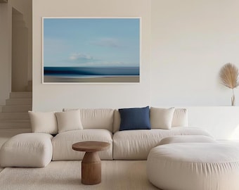 May include: A white sectional sofa with a blue throw pillow, a wooden coffee table, and a white ottoman in a modern living room with a framed abstract seascape painting on the wall.