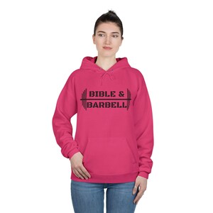 May include: A magenta hoodie with a drawstring hood and a front pocket. The black text "BIBLE & BARBELL" is printed on the front, with a barbell graphic. The model is wearing blue jeans.
