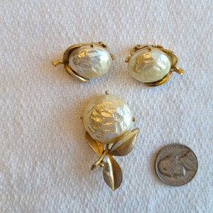 May include: A vintage jewellery set comprising a brooch and matching clip-on earrings. The set features a large, textured faux pearl with gold-tone leaf accents. A nickel coin is included for size reference.
