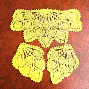May include: A set of three handmade, bright yellow crochet doilies. The largest piece is rectangular with a scalloped edge, and the two smaller pieces are fan-shaped. The intricate design features a repeating heart pattern.