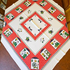 May include: A square tablecloth featuring a white center and a wide red brick-patterned border. The design includes illustrations of spinning wheels, grandfather clocks, scales, and carts with yellow flowers, arranged in a repeating pattern.