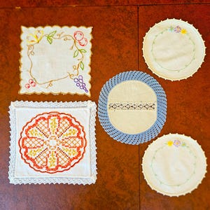 Peut inclure: Ensemble de dessous de verre et de napperons brodés à la main. L'ensemble comprend des pièces carrées et rondes avec des motifs floraux et géométriques. Les couleurs incluent le blanc, le jaune, l'orange, le violet et le bleu. Les bords sont finis avec de la dentelle ou du crochet.