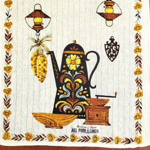 May include: A vintage kitchen towel with a retro design. The towel features a black coffee pot with yellow floral accents, a wooden coffee grinder, and a bowl. The border has yellow flowers and brown leaves. The text "ALL PURE LINEN" is visible.