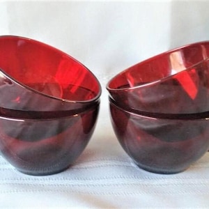 May include: A set of four deep red translucent glass cups with rounded bowls and curved handles. Two cups are stacked on the left side, while the other two are stacked on the right side, showcasing the vibrant ruby-colored glass material.