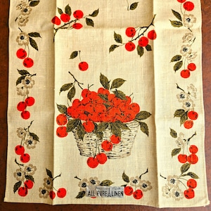 May include: A cream-colored linen towel with a vibrant cherry design. A basket overflowing with red cherries is the focal point, surrounded by cherry branches and floral accents. The towel has a border of cherries and flowers.