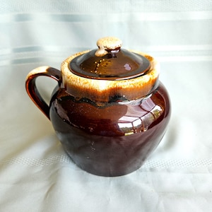 Peut inclure: Un sucrier en céramique marron avec un couvercle. Le bol a une poignée et une finition brillante. Le bord et le bouton du couvercle sont de couleur beige clair. Le sucrier est probablement vintage ou antique.