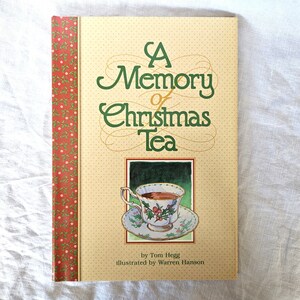 May include: A book titled "A Memory of Christmas Tea" with a cream-colored cover featuring green text and a teacup illustration. The spine has a red and green floral pattern. The book is by Tom Hegg and illustrated by Warren Hanson.