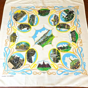 May include: Cream-colored vintage souvenir tablecloth featuring illustrations of various landmarks in a circular pattern. The illustrations are framed in blue and yellow, with a decorative border. Text includes "EXCLUSIVE TO D.M. BROWN."