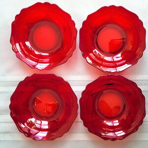 May include: Four red glass bowls with a scalloped edge and a central circular indentation. Each bowl has a dark, star-like design around the centre. The bowls are arranged in a square formation.
