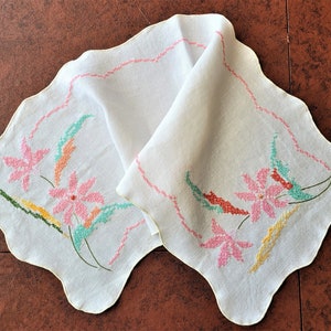 May include: White embroidered handkerchief with a scalloped edge. The handkerchief features pink, green, and yellow floral cross-stitch embroidery. A pink cross-stitch border trims the edge of the handkerchief.