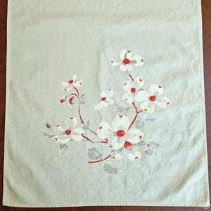 May include: A light green tea towel with a floral design. The design features white flowers with red centers and gray leaves and stems. The tea towel is made of a soft, textured fabric.