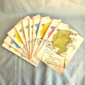 May include: A collection of vintage sewing and sampling books. The covers feature the title "Simplified Systems of Sewing and Sampling" with colorful abstract designs. The books are fanned out, showcasing their aged paper and retro aesthetic.