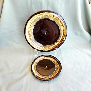 May include: Two ceramic plates with a dark brown center and a cream and brown rim. The plates are round and have a glossy finish. One plate is larger than the other. The plates are displayed on a light blue surface.