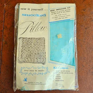 May include: A vintage smocked pillow kit in a clear plastic package. The package features text that reads "sew it yourself... smocked Pillow" and "very easy to make." The kit includes fabric, pattern, thread, cording, welting, and instructions.